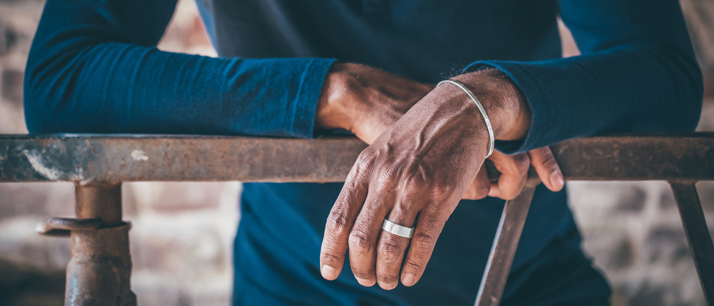 Ellenbogen auf einem Geländer abgestützt und Hände übereinander gelegt. Die obere Hand trägt einen Ring und einen Armreif aus Silber. Die Oberfläche der Schmuckstücke ist mit einer Hammerschlagsturktur versehen.