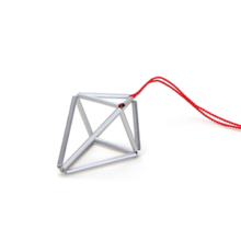 Anhänger Prisma klein, silberfarben Silberfarbener Anhänger an roter Seidenschnur. Der Anhänger prisma beschreibt einen ungleichseitigen Doppeltetraeder, der an Kristall erinnert. Er ist aus eloxierten Aluminiumröhrchen, die unsichtbar auf Nylon aufgezogen die Seitenkanten des Polyeders bilden.
