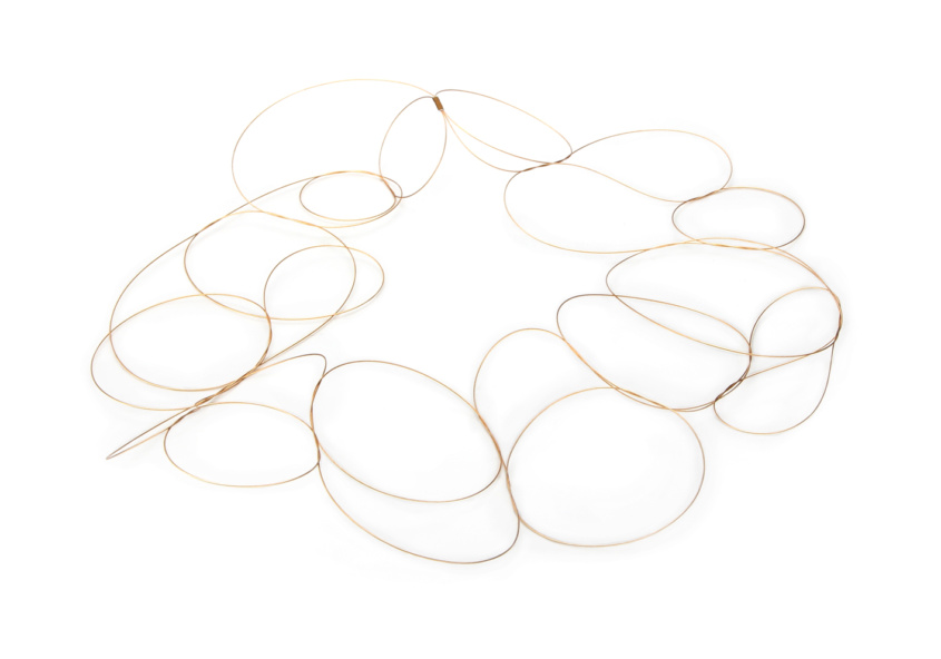 Drei Nylon ummantelte und vergoldeten Drahtsaiten sind zu luftigen Schlaufen miteinander verflochten und erzeugen ein feines Gewebe, welches wie ein zarter Film auf der Kleidung getragen werden kann.