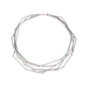Fünfreihige Kette aus unterschiedlich langen Aluminiumröhrchen. Die Röhrchen sind auf rote Perlseide geknotet. Die Knoten erscheinen wie rote Perlen in den Zwischenräumen. Die Kette wird durch einen zylindrischen Magnetverschluss geschlossen.