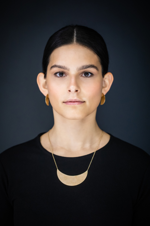 Anhaenger-und-Ohrstecker-moon Frau mit dunklem Haar, streng nach hinten gebunden in frontal Ansicht. Um den Hals trägt sie ein feines Kettchen mit einem großen Anhänger in From einer liegenden Mondsichel. Om Ohr Stecker in Form von Halbkreisen. Sie werden erst aus der Seitenansicht richtig sichtbar. Alles Stücke sind aus vergoldetem Silber gearbeitet.