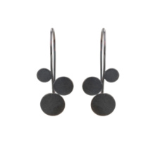 Pair of earrings made from blackened sterling silver. Three circular plates of different sizes are arranged asymmetrically but mirror-image along a wire. The largest tile hangs like a drop at the end, the other two are offset to the left and right. The continuation of the wire is bent back towards the ear hook.