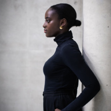 Ohrstecker-GAP-golden Frau lehnt mit dem Rücken gegen eine Säule. Sie trägt goldfarbenen Ohrschmuck in Form von Kreisscheiben. Diese sind bis zur Mitte eingeschnitten, so dass durch auseinander biegen eine räumliche Wirkung entsteht. Eine Spitze sitzt auf dem Ohrläppchen, die andere ihr gegenüber ragt dahinter.