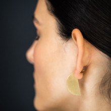 Frauenkopf im Profil mit vergoldetem Ohrstecker. Dieser beschreibt eine Halbkreisscheibe, 30mm im Durchmesser. Der Ohrschmuck ist so getragen, dass der Halbkreis im Profil, also von der Seite zu sehen ist.