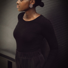 Ohrstecker-und-Ring-big-disk Frau lehnt mit dem Rücken an einem Geländer vor einer dunklen Wand. Den Daumen ihrer linke und sichtbaren Hand hat sie so in die Hosentasche gesteckt, dass der Rest der Hand sichtbar ist. Auf dem Ringfinger trägt sie einen großen Ring. Im linken Ohr einen auffälligen Ohrstecker. Beide Schmuckstücke haben eine 30mm Kreisplatte aus geschwärztem Silber, welche mit roter Seide in Form von drei Linien bespannt sind.