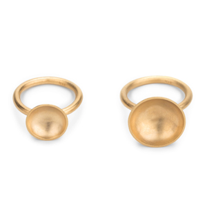 Zwei Ringe mit unterschiedlich großer Schale auf 3mm starker Ringschiene aus Runddraht liegen nebeneinander. Die Ringe sind aus Silber gearbeitet und vergoldet.