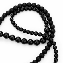chain-onyx-round-close Part of a long onyx ball chain. Three different sizes of balls are lined up in a row and are matt or glossy.