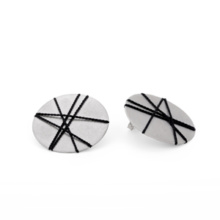 The discs made of silver measure 30mm, which are made here as ear studs. A graphic pattern is stretched over the surfaces with black silk ribbon.