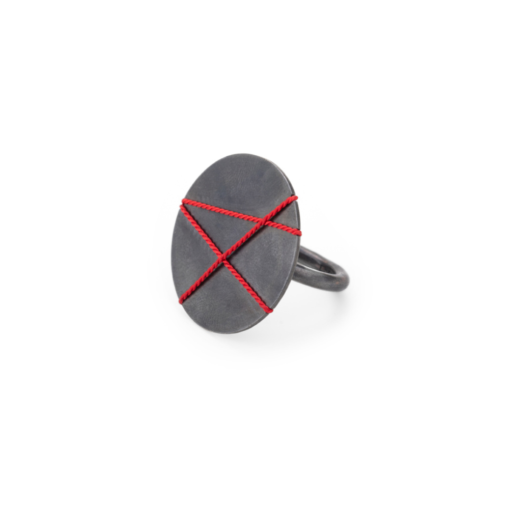 Ring with large 30mm decorative plate made of blackened silver. The plate is covered with three red, overlapping lines of silk, which creates a graphic pattern