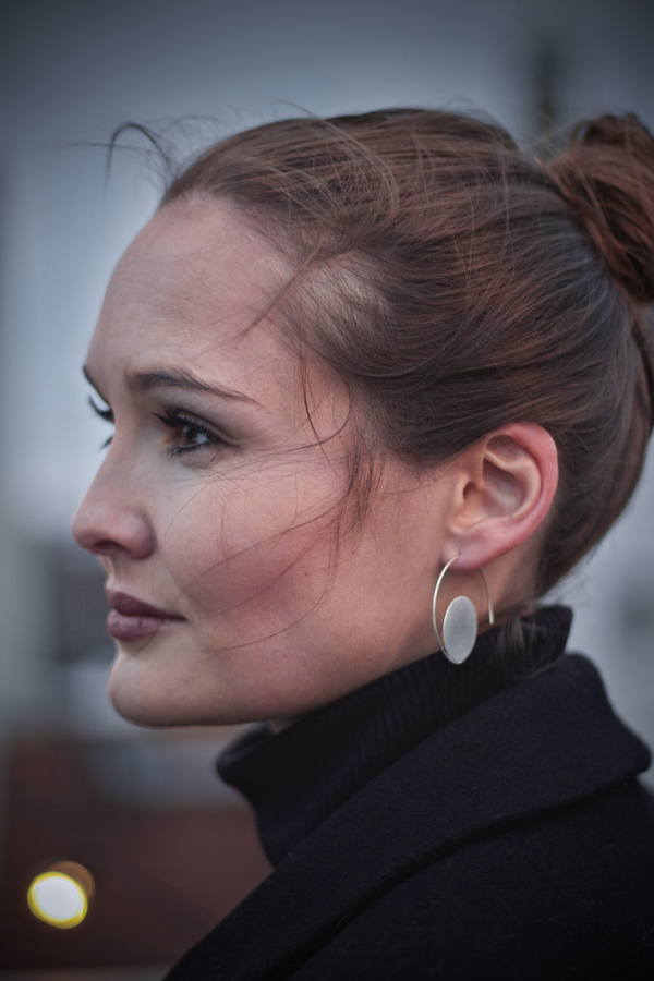 creole-SUN Frau im Profil mit Silberohrschmuck. Eine Silberscheibe von 22mm Durchmesser scheint fast zu schweben. Fast wie eine Spirale läuft ein Runddraht um die Scheibe, welcher auch gleich die Funktion erfüllt. Der Draht wird wie bei einer Creole durch das Ohrloch gesteckt.