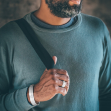 Männerhand mit einem eleganten, silbernen Armreif und einem Silberring geschmückt. Der Armreif ist etwa 15mm breit und mit einem feinen Strichmatt überzogen.