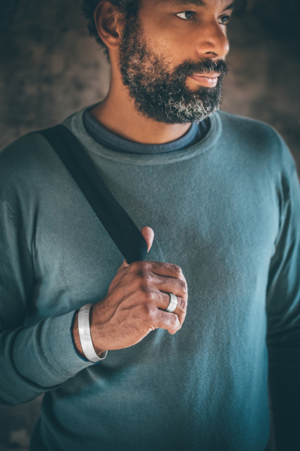 Männerhand mit einem eleganten, silbernen Armreif und einem Silberring geschmückt. Der Armreif ist etwa 15mm breit und mit einem feinen Strichmatt überzogen.