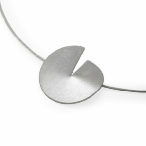 A circular pendant made of silver suspended from a string. The pendant disc is cut to its center, the corners slightly bent apart to create a slit and the pendant becomes three-dimensional