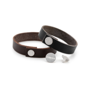 Two leather bracelets with silver buttons. These are stamped with words. Two more silver buttons lie in front of it. One also labelled, the other shown from the back.