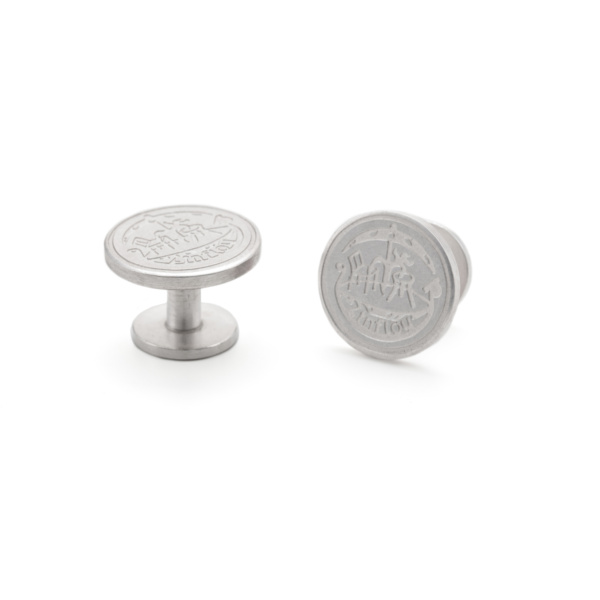 One standing and one lying cufflink in silver. They resemble a coil because a cylindrical pin connects two circular plates. The larger plate is engraved with a coat of arms and is the decorative plate.