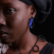 Nahaufnahme einer Frau, die mit blau schwarzen Ohrsteckern aus Onyx- und Achatperlen und einer Onyxkette geschmückt ist.
