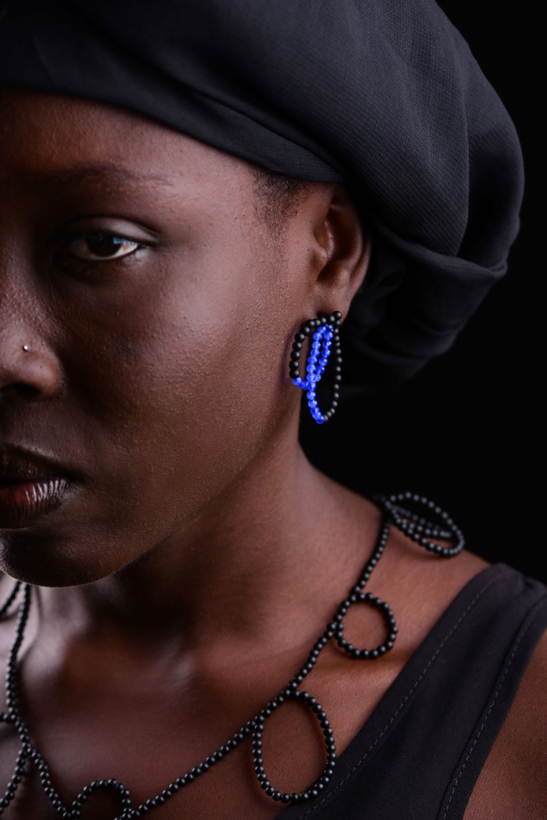 Nahaufnahme einer Frau, die mit blau schwarzen Ohrsteckern aus Onyx- und Achatperlen und einer Onyxkette geschmückt ist.