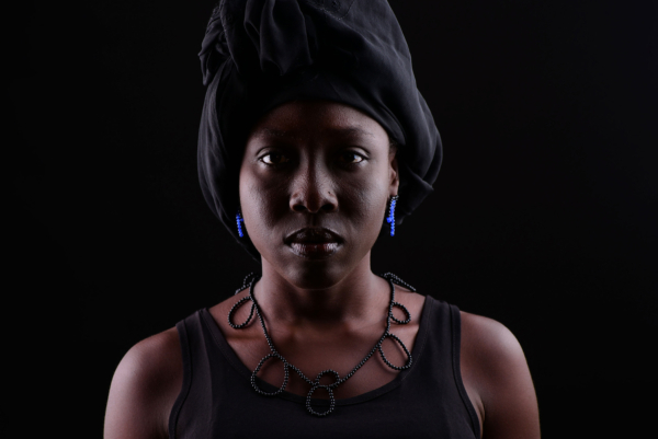 kette_capreolo_ohrst_tendrilblau Frau mit Kette und Ohrschmuck aus kleinen Onyxperlen. Diese sind so geknüpft, dass unterschiedlich große Zier-Schlaufen entlang der Kette entstehen. Der Ohrschmuck ist zusätzlich aus blauen Achatperlen. Die Schwarzen und blaue Perlen sind zu zwei Schlaufen auf Nylon aufgezogen und mit einem Stecker aus Silber versehen.