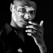 ring_COUBO_brosche_carre Ein Mann trägt einen Ring und eine Brosche. Beide Stücke sind quadratisch aus geschwärztem Silber gearbeitet und mit einem quadratischen, kristallisierten Onyx besetzt.