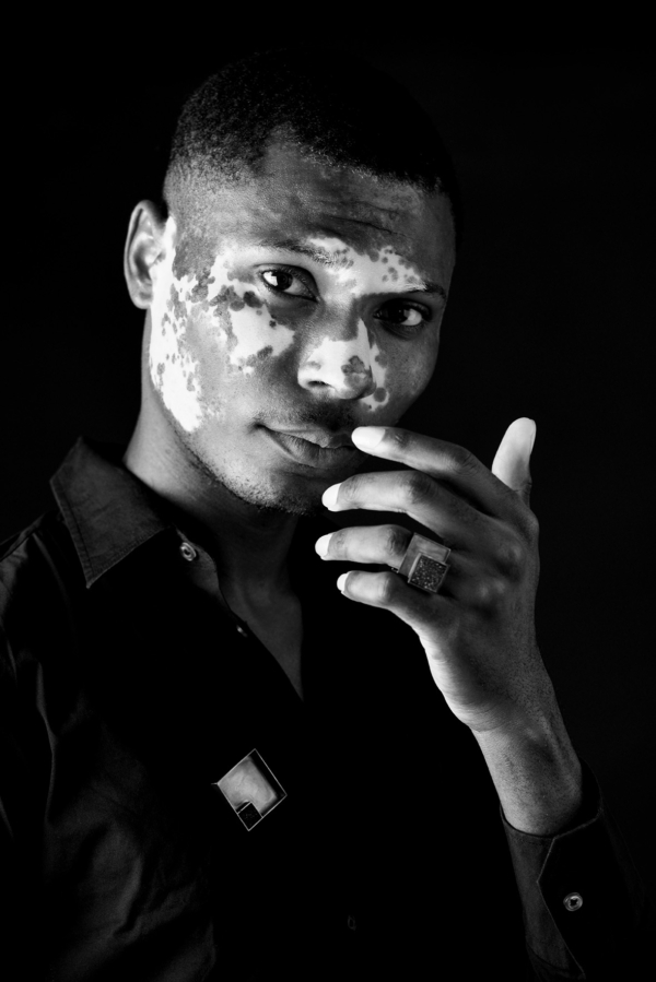 ring_COUBO_brosche_carre Ein Mann trägt einen Ring und eine Brosche. Beide Stücke sind quadratisch aus geschwärztem Silber gearbeitet und mit einem quadratischen, kristallisierten Onyx besetzt.