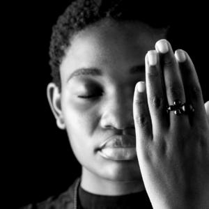 Eine Frau hebt ihre Hand vor ihr Gesicht. An dieser trägt sie einen schwarzen Silberring mit unterschiedlich großen Kugeln verziert, aus Onyx und Hämatit.