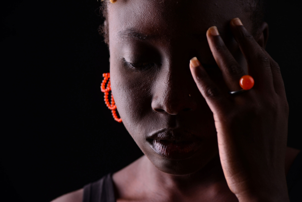 ring_sphere_karneol_ohrst. capreolo_karn A woman with a vibrant orange ring and Carnelian earrings. The ring is made of blackened silver with a Carnelian bead, while the earrings are crafted from small Carnelian beads threaded into loops.