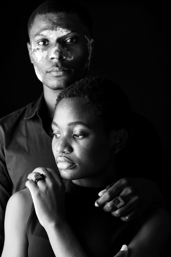 ringe_COUBO+carre Ein Mann steht hinter einer Frau. Beide tragen quadratische Ringe mit kristallisierten, quadratischen Onyx-Steinen besetzt.