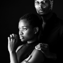 ringe_carre_ring_COUBO Ein Mann steht hinter einer Frau. Beide tragen eckige, schwarze Ringe mit quadratischen Onyxsteinen besetzt.