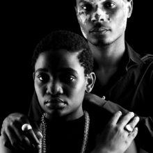 ringe_paar_konkavkonvex_rund Ein Mann und eine Frau stehen hintereinander. Beide tragen Siegelringe mit runder Siegelplatte. Der Männerring ist konvex, der Frauenring konkav gewölbt. Die Frau trägt eine Kette aus Bergkristallkugeln.