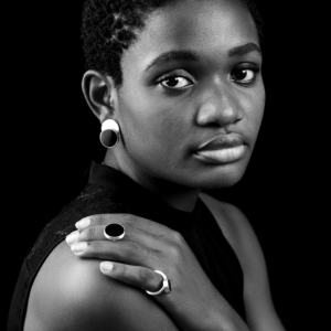 Eine Frau blickt in die Kamera, Hand auf der Schulter. Sie trägt Ohrstecker und zwei Ringe aus Silber mit großen Onyxscheiben verziert.