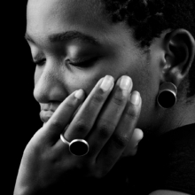ring+ohrst_laminam_onyx_close Close-up of hand and head of woman wearing ring and earring made of silver, decorated with large onyx discs.