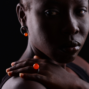 A woman wearing a ring stud earring with an orange pearl on her ear and an orange pearl ring on her finger.