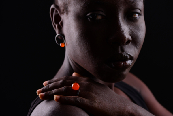 A woman wearing a ring stud earring with an orange pearl on her ear and an orange pearl ring on her finger.